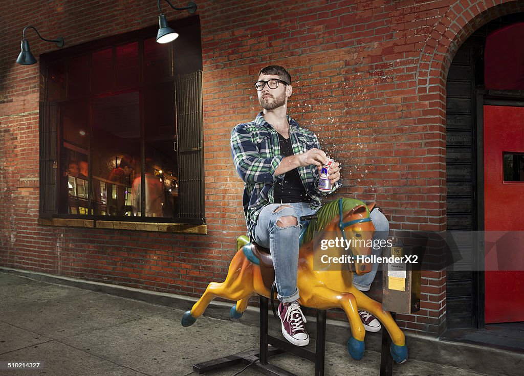 Hipster Man on mechanical horse drinking beer