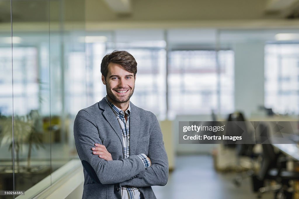 Happy businessman standing arms crossed in office