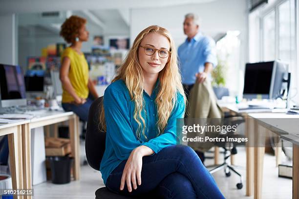 smiling businesswoman sitting at creative office - three quarter length stock pictures, royalty-free photos & images