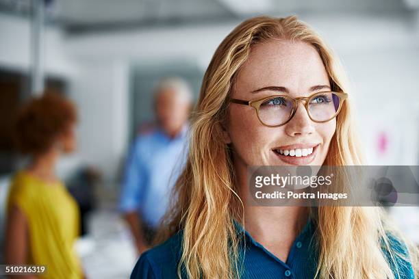 thoughtful businesswoman smiling in office - bril brillen en lenzen stockfoto's en -beelden