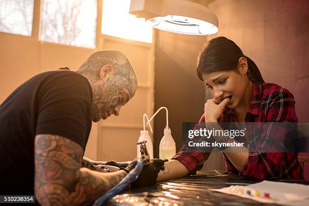 nervous woman getting her arm tattooed in tattoo studio. - tattooing stock pictures, royalty-free photos & images