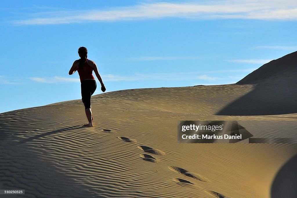 Woman running up sand dunes in Huacachina Desert