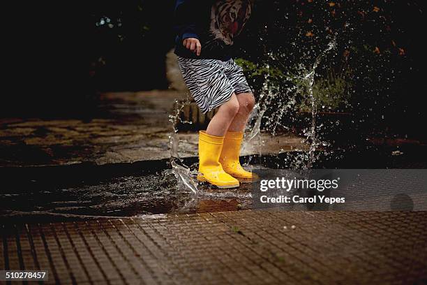 boy splashing in a puddle - charco fotografías e imágenes de stock