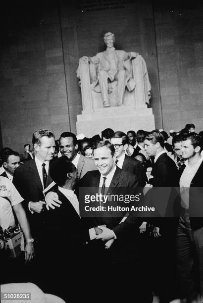 American actor Marlon Brando stands with his arm around poet James Baldwin, surrounded by actors Charlton Heston , Harry Belafonte and others...