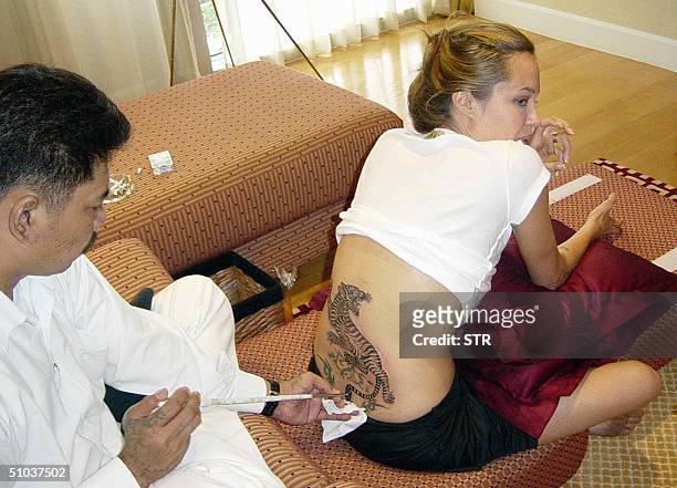 Hollywood superstar Angelina Jolie smiles while getting a tattoo from Thai tattoo master, Sompong Kanphai at an apartment in Bangkok, 08 July 2004....