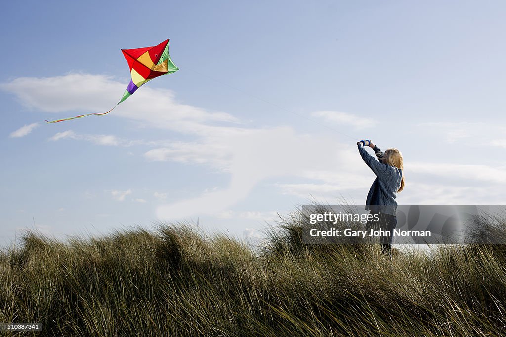 Teenage girl flying a kite on the beach.