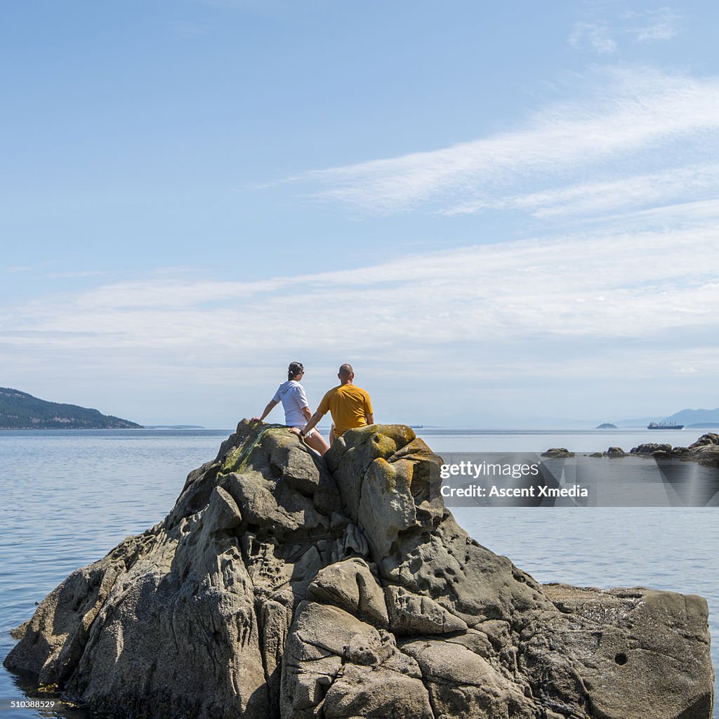 Couple stand on rock island, enjoying sea view