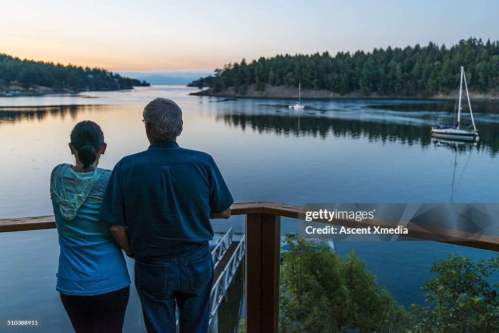 Senior couple look across calm ocean bay, veranda