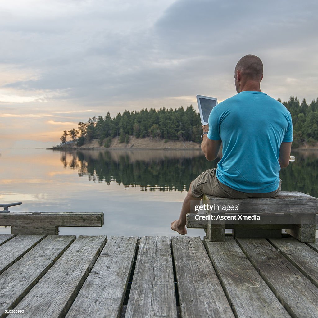 Man uses digital tablet on seaside pier