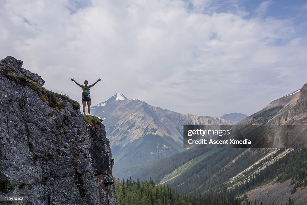 Female hiker stands with arms outstretched, mtns