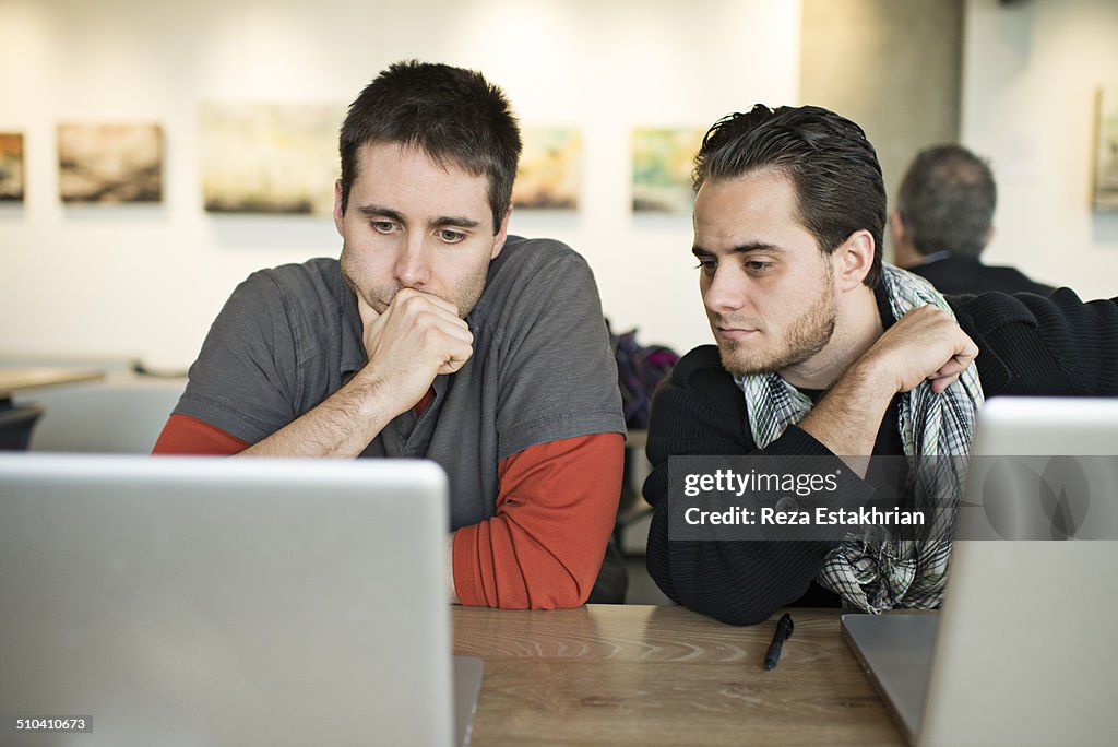 Two men in cafe brainstorm over laptop