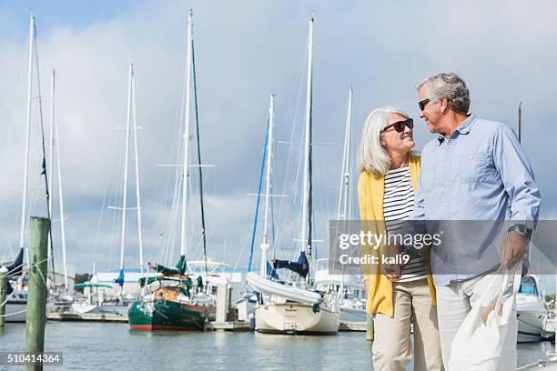 happy senior couple walking along harbor holding hands - marina stock pictures, royalty-free photos & images