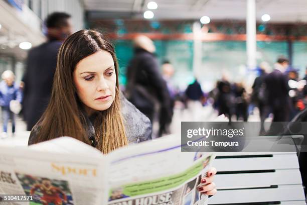 young woman reading the newspaper on a train station. - newspapers uk stock pictures, royalty-free photos & images