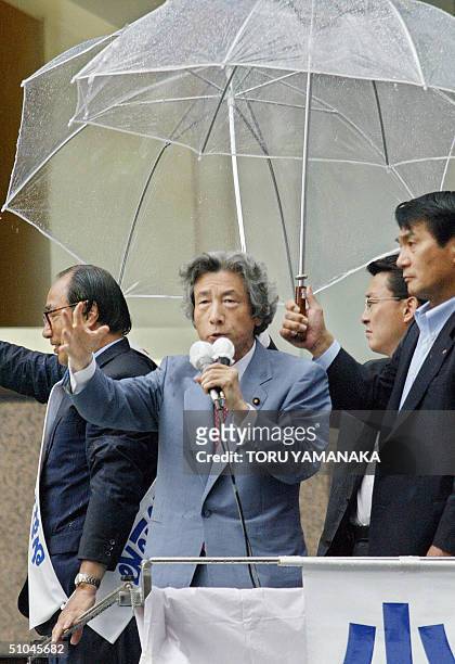 Two plainclothes policemen hold umbrellas as Japanese Prime Minister Junichiro Koizumi delivers a speech in support of cadidate of the ruling Liberal...