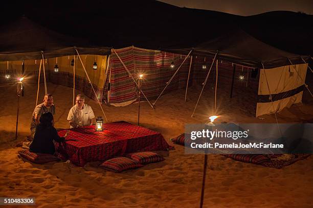 middle eastern and multi-ethnic friends enjoying conversation at desert camp - arabia travel stock pictures, royalty-free photos & images