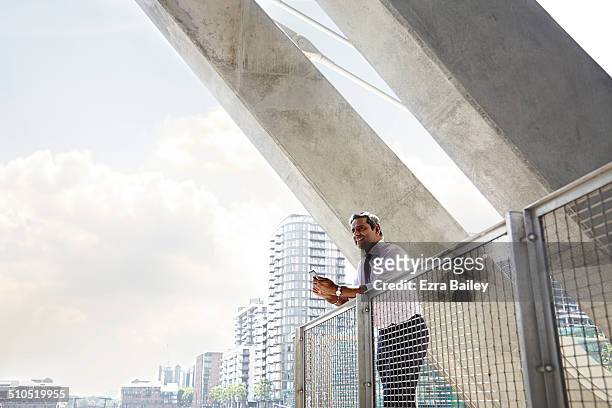 a businessman looking out over the city with phone - the bigger picture stock photos et images de collection