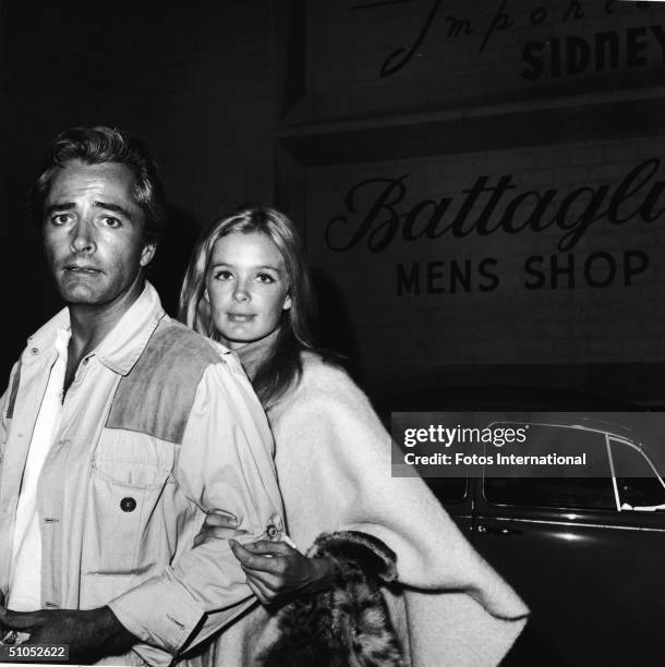 American film director John Derek and his wife, actor Linda Evans, look at the camera while standing outside a men's clothing shop, July 1967.