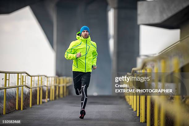 hombre deportista correr sobre el puente - abrigo verde fotografías e imágenes de stock