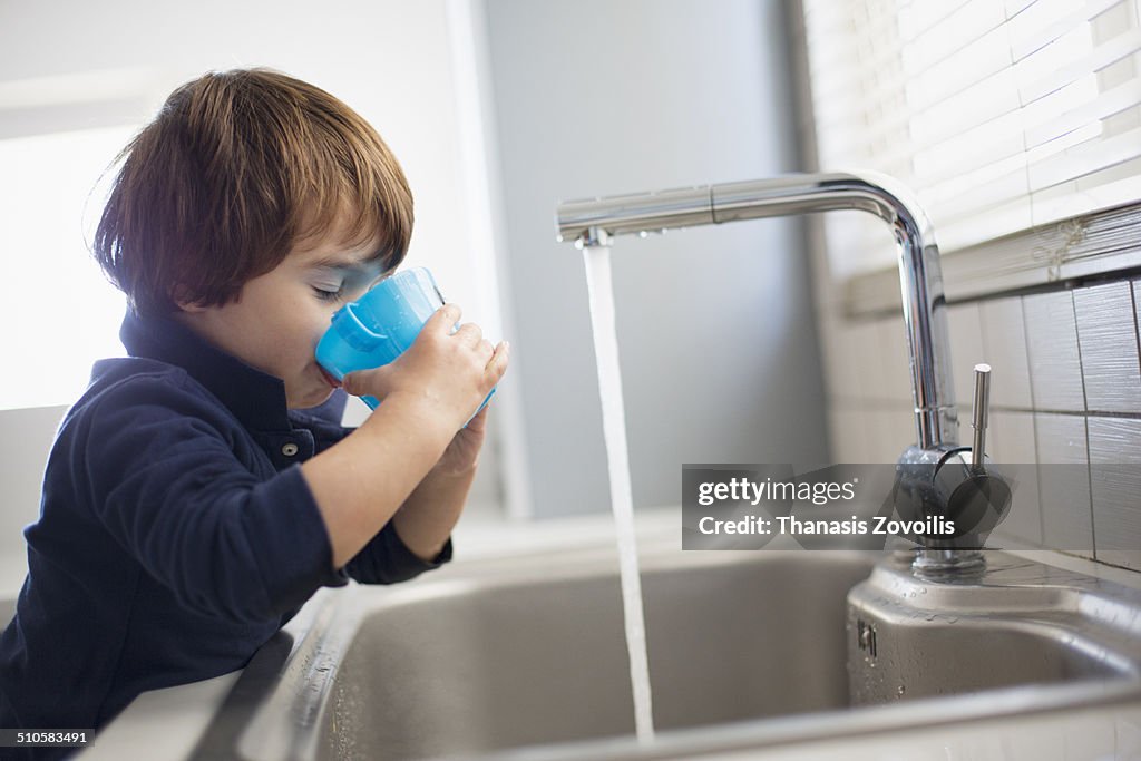 Small boy drinking water in the kitchen