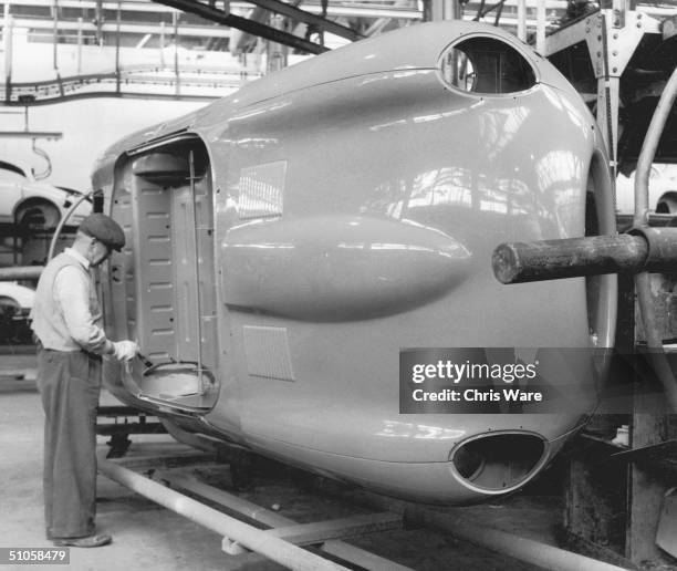 Worker touches up the paintwork on an E-Type Jaguar body shell at the company's Coventry works, 25th May 1961.