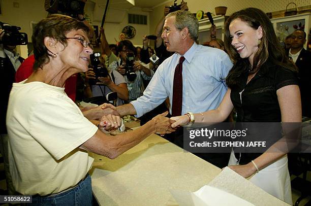 President George W. Bush he buys a bag of bear claws, during an impromptu stop on his Bus campaign tour, as his daughter Barbara shakes hands with...