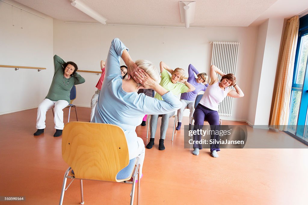 Teacher and active senior women yoga class on chairs