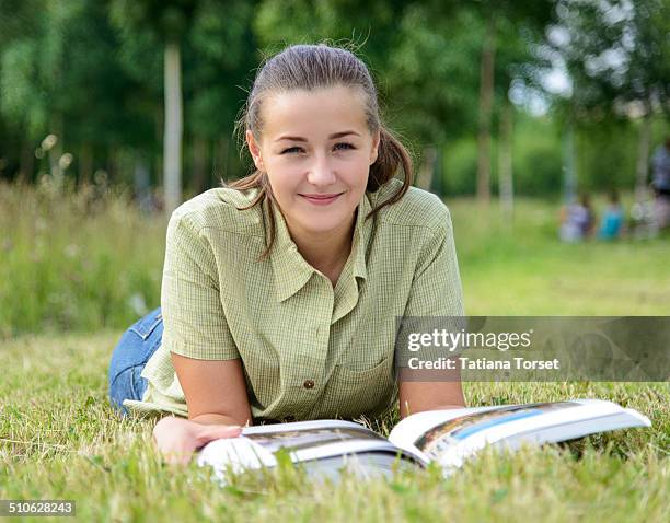 student girl reading a big book sitting on grass - short sleeved stock pictures, royalty-free photos & images