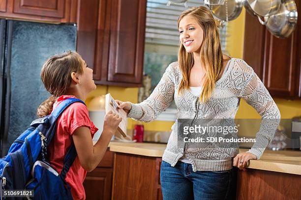 mom handing book to daughter as she leaves for school - giving a girl head stock pictures, royalty-free photos & images