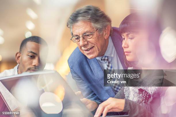más hombre ayudando a la joven con sus colegas en un ambiente tranquilo - old man young woman fotografías e imágenes de stock