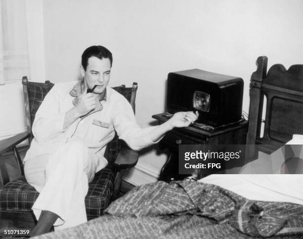 Man enjoys a peaceful pipe whilst listening to the radio in his pyjamas, circa 1940.