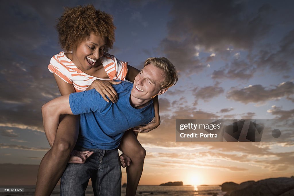 Man piggybacking woman on beach at sunset