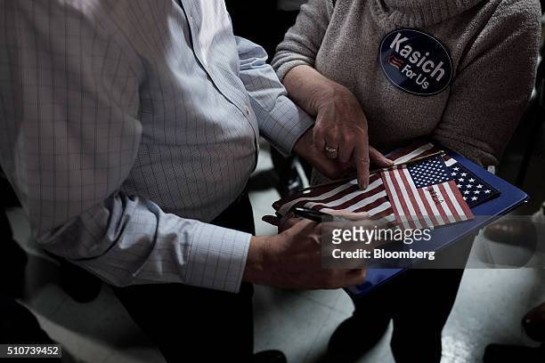 John Kasich, governor of Ohio and 2016 Republican presidential candidate, signs American flags for an attendee during a town hall event at Murray's...