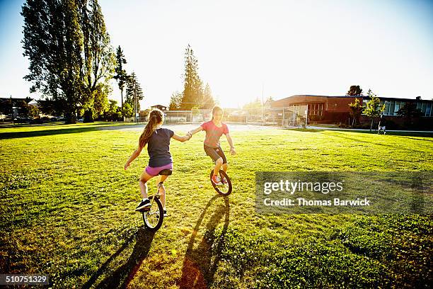 two girls holding hands riding unicycles in circle - unicycle stock pictures, royalty-free photos & images