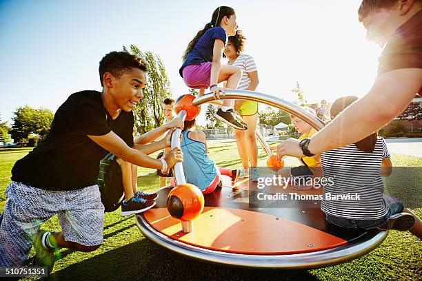 group of kids playing on merry go round - childrens playground foto e immagini stock