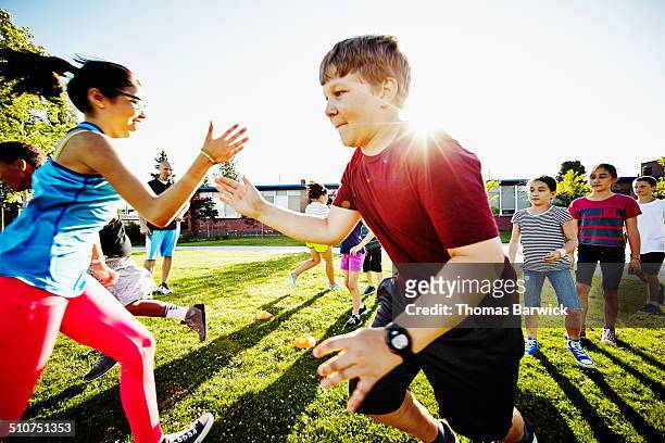 girl tagging boy in relay race on grass field - team event ストックフォトと画像