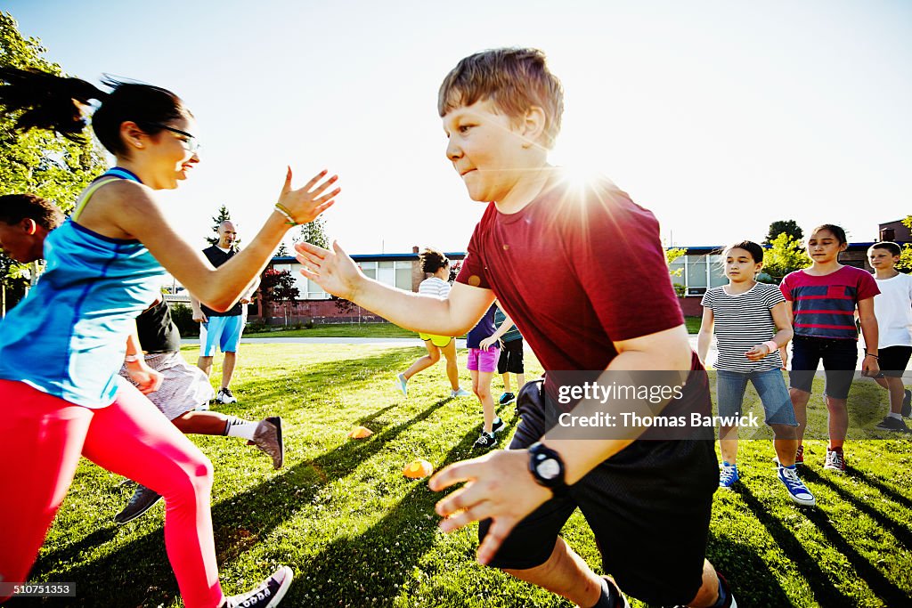 Girl tagging boy in relay race on grass field