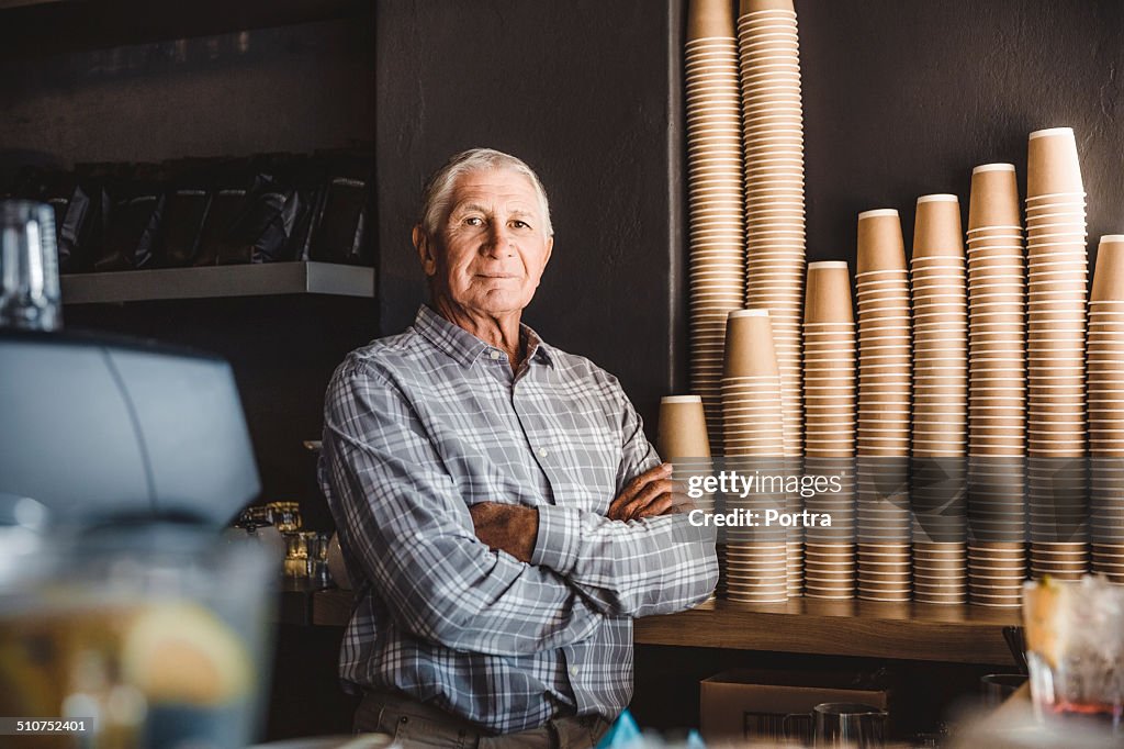 Confident senior owner standing at cafe