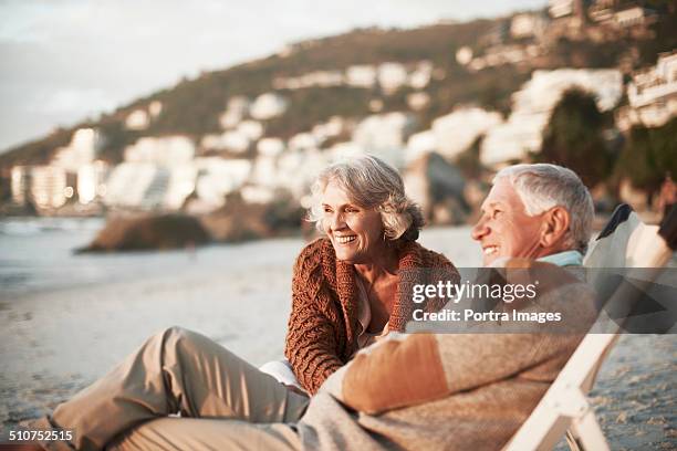 happy couple relaxing on chairs at beach - pensioen thema stockfoto's en -beelden