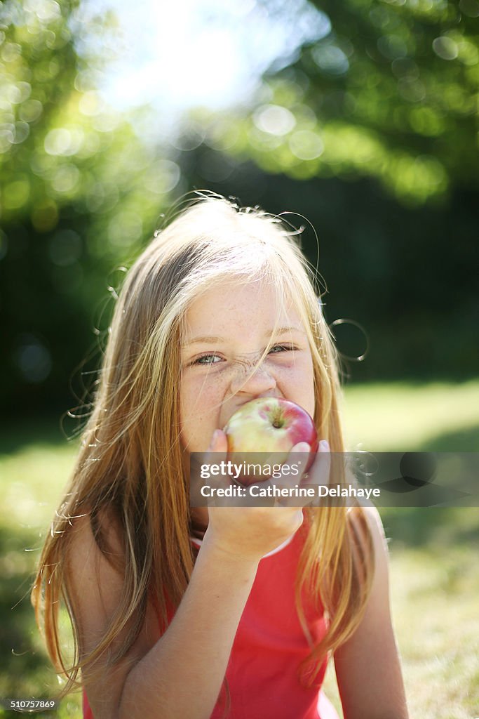 A girl eating an apple in a garden