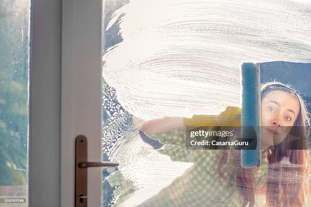 Frau Waschen Glastür mit Gummischrubber und Spähen durch Fenster