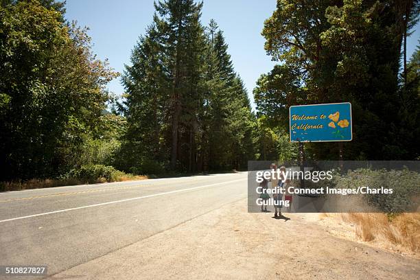 family standing at roadside by sign saying welcome to california - berma da estrada imagens e fotografias de stock