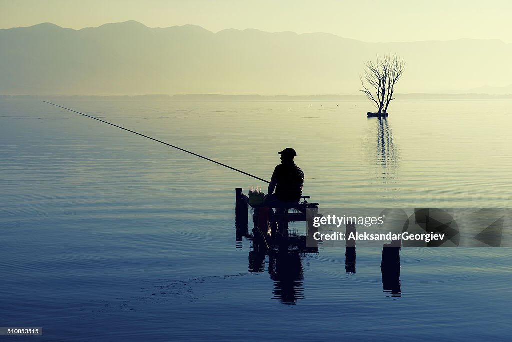 Silhouette of Man Fishing on The Lake at Sunrise