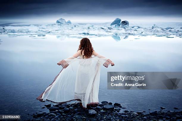 rear view of young woman in vintage sheer white nightgown standing at edge of jokulsarlon glacial lagoon, arms outstretched - see through negligee stock pictures, royalty-free photos & images