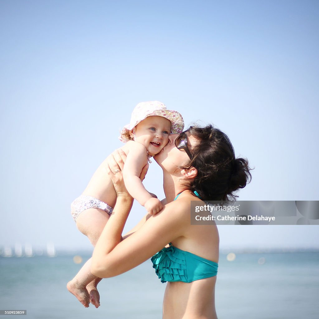 A mom kissing her baby girl on the beach