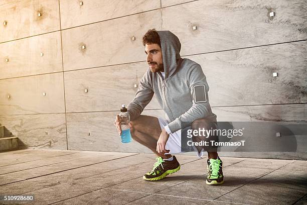athlete crouched with a sport drink - baanevenement mannen stockfoto's en -beelden