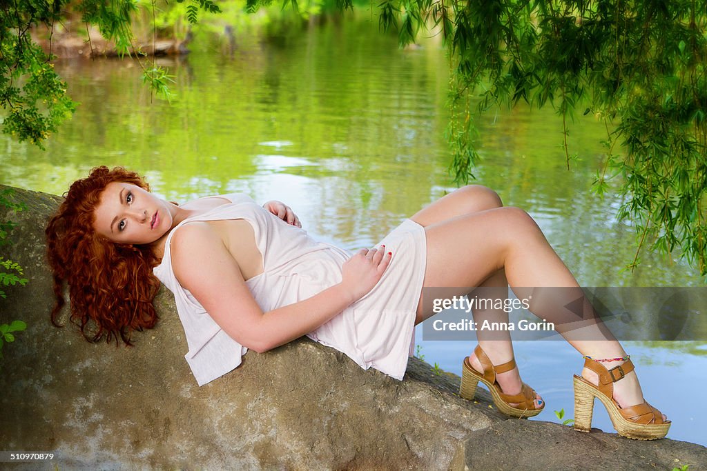 Beautiful teen redhead in dress reclining by water