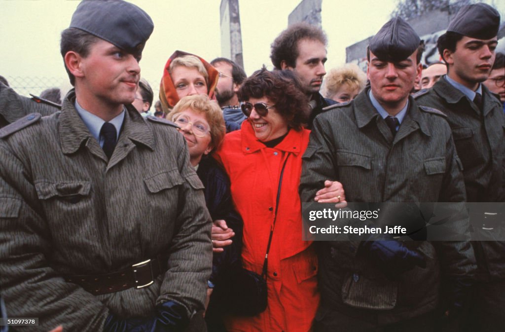 Two West German Women Hold The Arms Of Two East German Guards At The Berlin Wall...