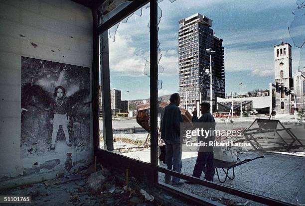 Two Sarajevans Take A Break During A Walk On War-Torn Streets, With Important Food And Water Supplies, Standing In The Shade And "Discussing News Of...