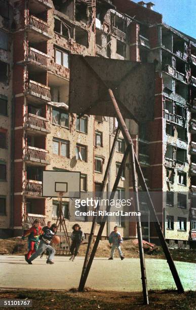 Kids Play Basketball At A Play Ground In Front Of Destroyed And Ruined Building Of Nigberdhod Alipasino Polje, A War Time Front Line, In Spring,...