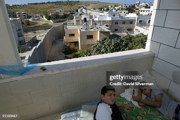 Palestinian boys escape from the summer heat in an unfinished house directly above Israel's separation barrier on July 21, 2004 as it slices its way...